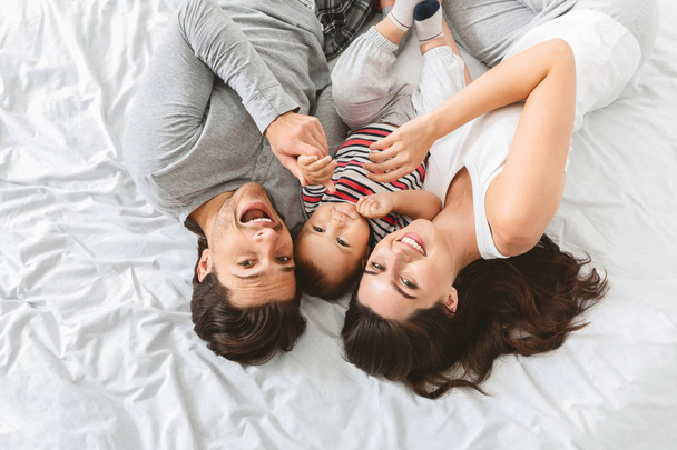 Fiatal férfi, nő és baba hozzábújva az ágyban együtt - Fotó, kép