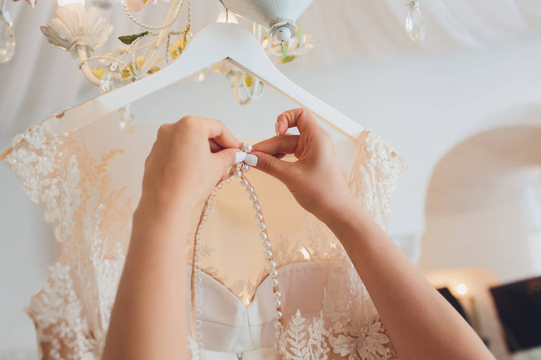 Rich pink wedding dress hangs on a chandelier in a white room. - 写真・画像