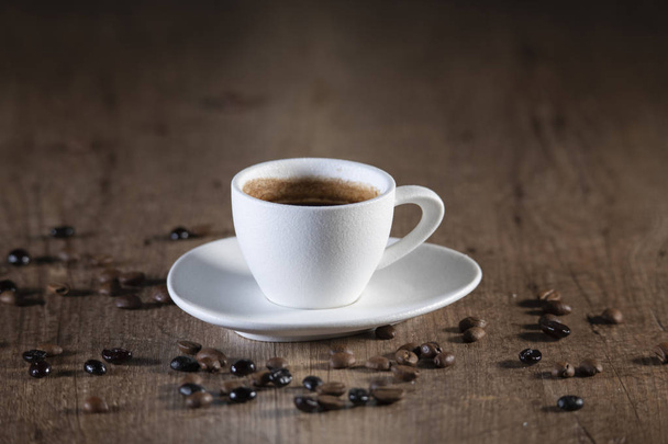 Pohled na bílý kávový pohár obklopen kávovou semínka na dřevěném stole - Fotografie, Obrázek