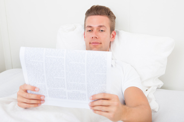 Young Man Lying On Bed Reading Newspaper - Foto, Imagen