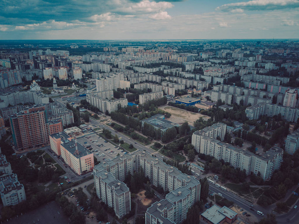 Aerial view of growing city in sunlight. Drone view of new building complex in city center with houses and roads under cloudy sky - Zdjęcie, obraz
