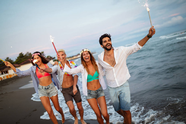 Group of friends lighting sparklers and enjoying freedom at beach during sunset - Photo, image