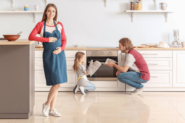 Young pregnant woman and her daughter with husband baking pastry in kitchen - Foto, imagen
