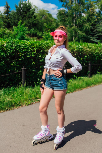 Portrait of an emotional girl in a pink cap visor and protective gloves for rollerblades and skateboarding riding on rollerblades on the road. - Valokuva, kuva