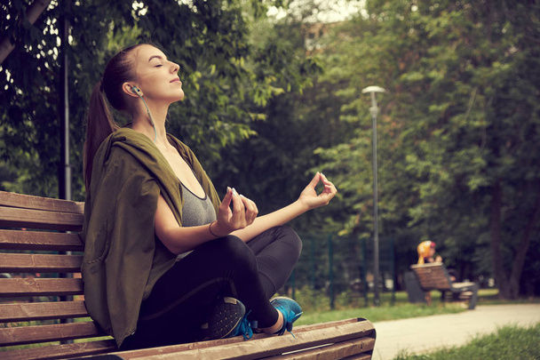 Young attractive female meditate in park. young woman resting in the lotus position in the park after a hard day - Photo, Image