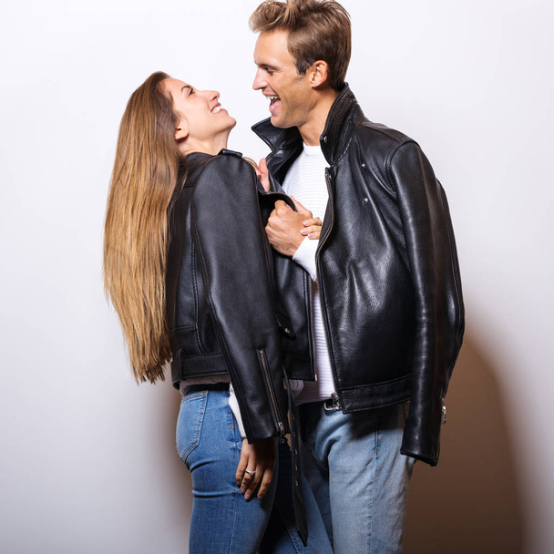 Young beautiful couple in black leather jackets pose in studio. - Фото, изображение