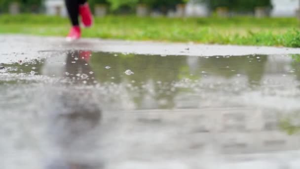 スニーカーのランナーの足。スポーツウーマンは屋外でジョギングをし、泥だらけの水たまりに足を踏み入れる。雨の中を走るシングルランナー、スプラッシュを作る - 映像、動画