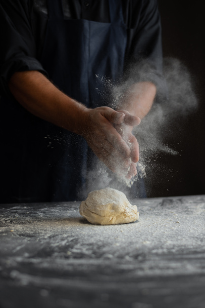 chef in the kitchen, male hands knead the dough, clap hands, a cloud of flour - Photo, Image