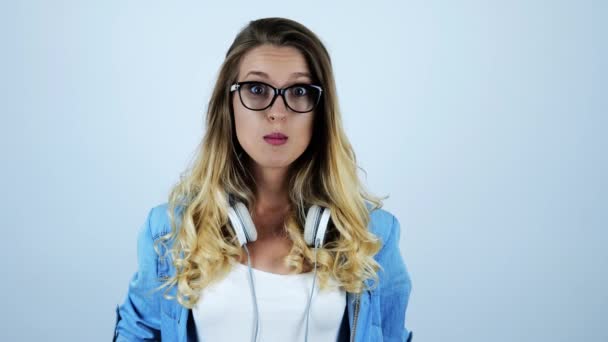 young beautiful blonde funny woman in eyeglasses inflating bubble gum with headphones on her neck on isolated white background - Video