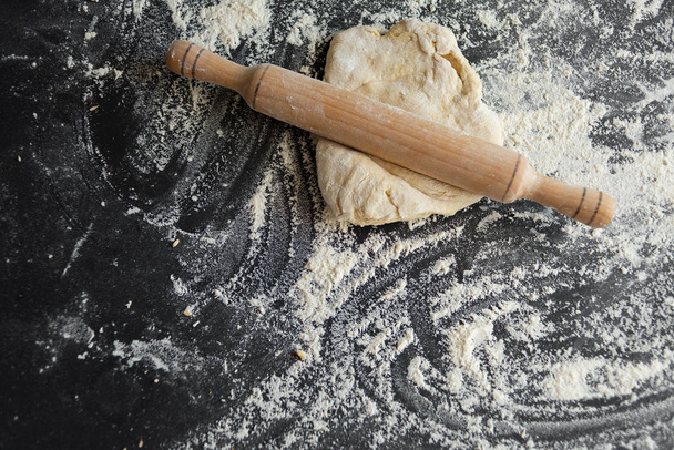 corteza de masa sobre un fondo negro, concepto de cocinar pizza, rodillo de madera
 - Foto, Imagen