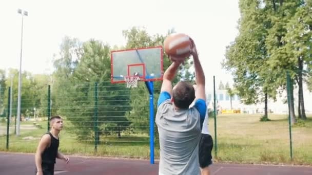 Junger Mann spielt mit Freunden Basketball auf dem Platz, wirft den Ball und verpasst den Korb - Filmmaterial, Video