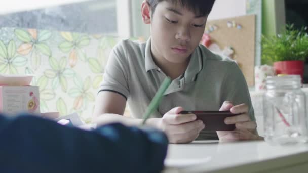 asiatischer Junge beim Hausaufgabenmachen mit Tablet-Computer, Teenager beim Lernen mit digitalem Tablet zu Hause mit Freund. - Filmmaterial, Video