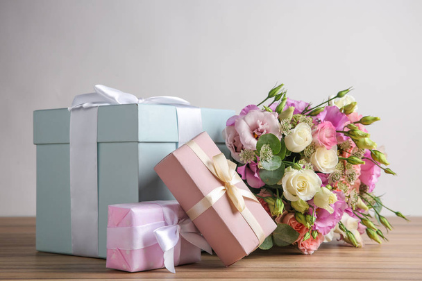 Beautiful bouquet of flowers and gift boxes on wooden table against light background - Fotoğraf, Görsel