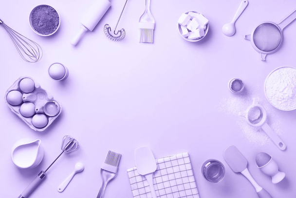 Bakery ingredients over trendy violet color background - butter, sugar, flour, eggs, oil, spoon, rolling pin, brush, whisk, towel. Baking frame, cooking concept. Top view, copy space. Flat lay - Fotó, kép