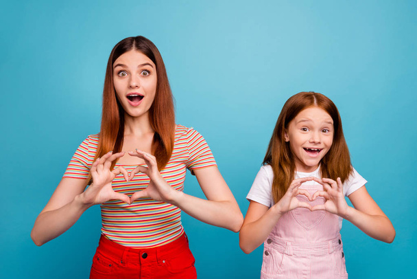 Pretty foxy little lady and her mom making heart figure with hands wear casual clothes isolated blue background - Foto, afbeelding