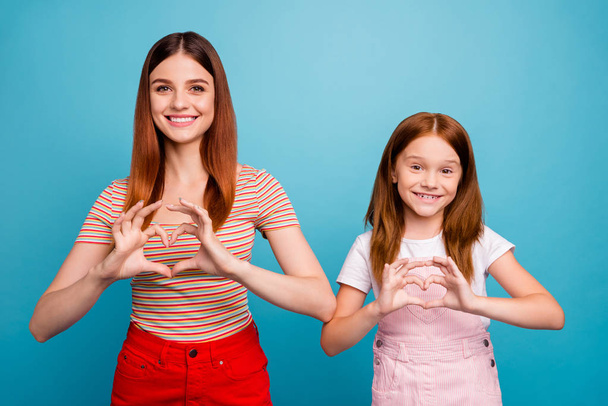 Pretty foxy little lady and her mom making heart figure with hands wear casual clothes isolated blue background - Фото, изображение