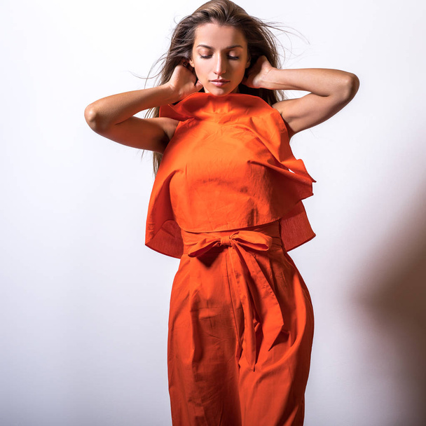 Young model woman in orange dress pose in studio. - Фото, изображение