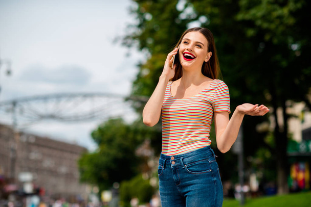 Portrait of cheerful woman with foxy ginger haircut red lips using gadget calling wearing striped t-shirt in town outside - Foto, Imagen
