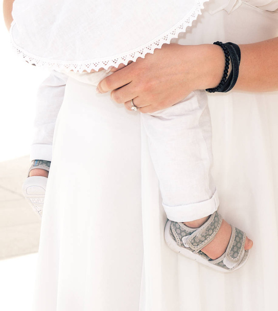 Concept of unity, support, protection and happiness.Maternity.Soft focus of baby leg and mommy hand,Mother hold her baby. Baptism.Christening.Body part.Mother hold baby boy during christening ceremony - Фото, изображение