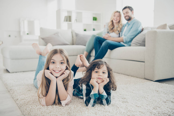 Foto de la familia grande dos niños cómodos piso tendido alfombra mullida, mientras que los padres se sientan sofá
 - Foto, Imagen