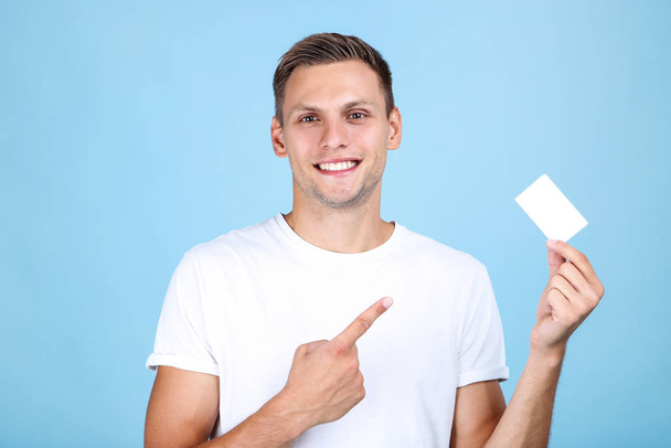 Young man with blank business card on blue background - Φωτογραφία, εικόνα