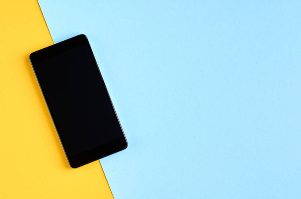 Black cellphone on yellow and blue background composition, mobile phone. - Photo, image