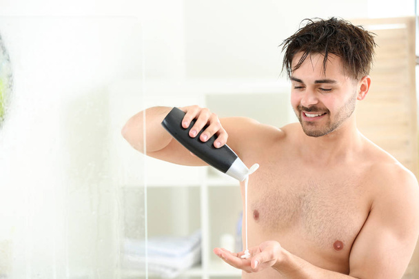 Красивый мужчина с бутылкой шампуня принимает душ дома
 - Фото, изображение