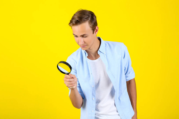 Young man with magnifying glass on yellow background - Photo, Image