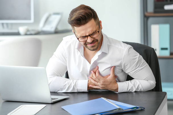 Young businessman having heart attack in office - Foto, afbeelding