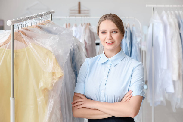 Worker of modern dry-cleaner's near rack with clothes - Foto, imagen