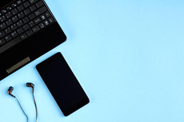 Black laptop keyboard, cellphone and headphones on blue background composition. - Photo, image