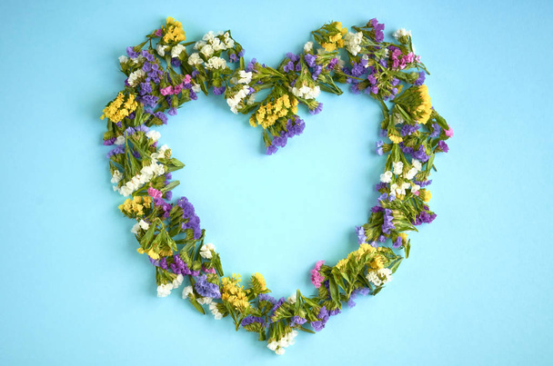 Mavi arka plan kompozisyonu, kalp şekli renkli çiçekler. Düz yatıyordu - Fotoğraf, Görsel