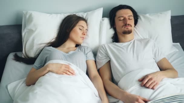 Młody atrakcyjny mężczyzna i kobieta śpiące w łóżku w domu spoczywają razem - Materiał filmowy, wideo