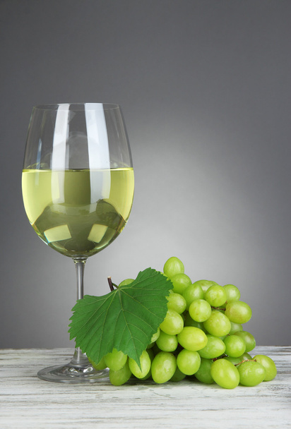 Ripe delicious grapes with glass of wine on table on gray background - Foto, Bild
