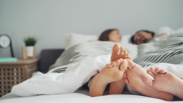Male and female feet touching in bed couple talking lying together under blanket - Video