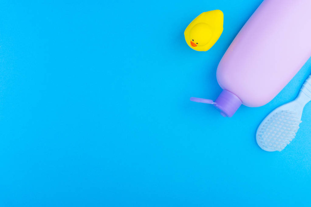 Flat lay composition of baby care products on a blue background. View from above shampoo or shower bottle gel, cleaning brush and yellow rubber toy duck - Photo, Image
