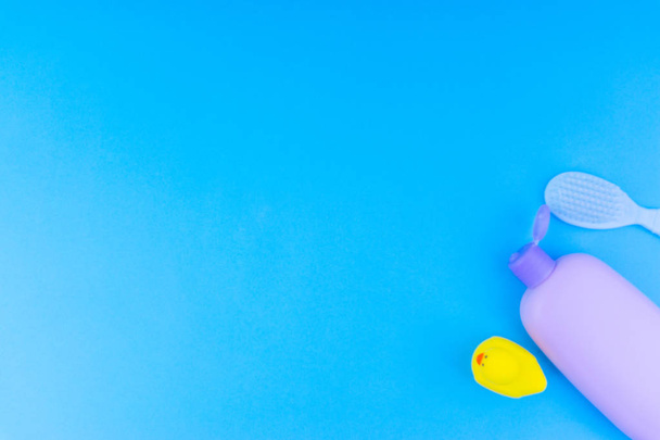 Unscharfe flache Komposition von Babypflegeprodukten auf blauem Hintergrund. Blick von oben Shampoo- oder Duschflaschengel, Reinigungsbürste und gelbe Gummispielzeugente - Foto, Bild