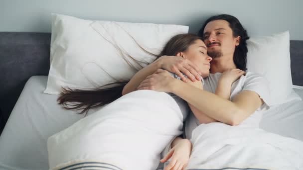 Man and woman couple are lying in bed hugging talking enjoying bedtime - Filmati, video