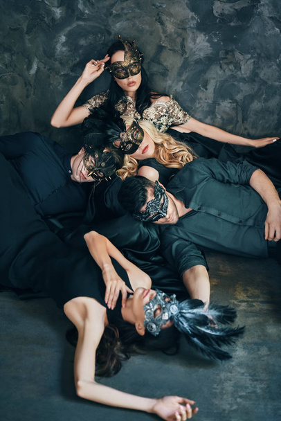 Group of friends in masquerade carnival masks laying on floor relaxing after party. Women and men wearing venetian masks. - Foto, Imagen