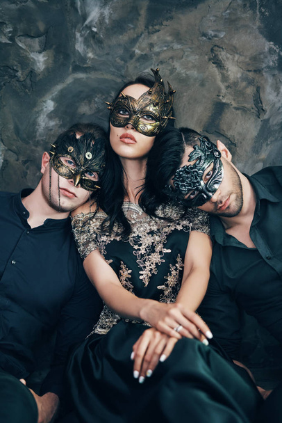 Woman with men in masquerade carnival masks laying on floor relaxing after party. - Фото, изображение