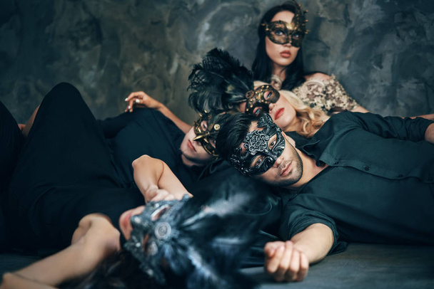 Group of friends in masquerade carnival masks laying on floor relaxing after party. Women and men wearing venetian masks. - Zdjęcie, obraz