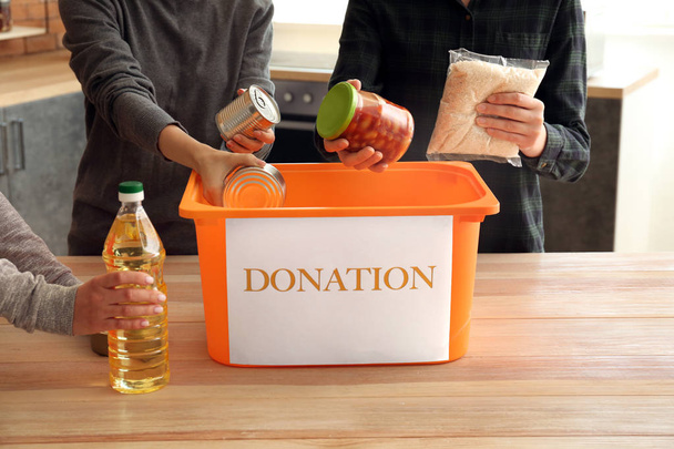 Ehrenamtliche packen gespendete Lebensmittel in Schachtel am Tisch - Foto, Bild