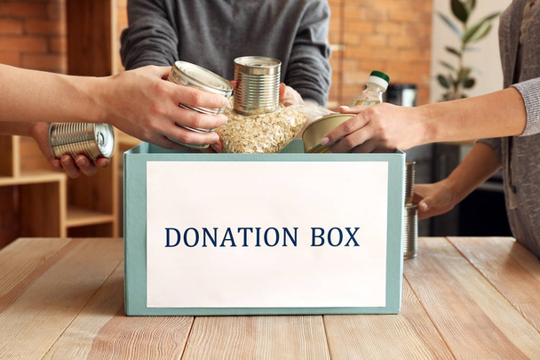 Добровольцы кладут еду для пожертвований в коробку за столом
 - Фото, изображение