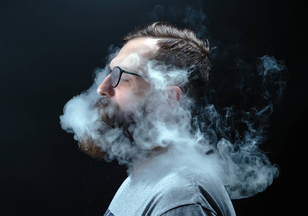 Concept. Smoke enveloped the head man. Portrait of a Bearded, stylish man with smoke. Secondhand smoke - Foto, afbeelding