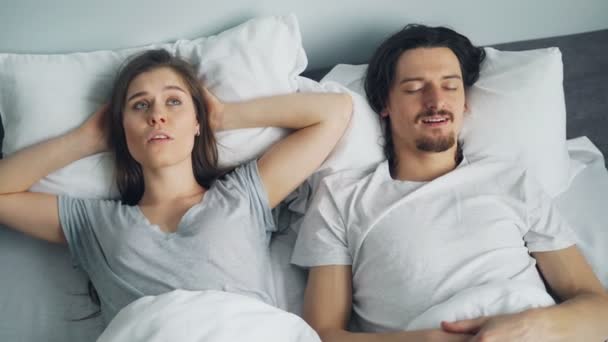 Unhappy girl covering ears with pillow while husband snoring in bed - Filmagem, Vídeo