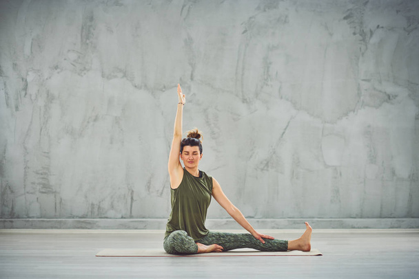 Bella bruna caucasica in abbigliamento sportivo verde seduta sul tappeto a piedi nudi e facendo esercizi di yoga
. - Foto, immagini