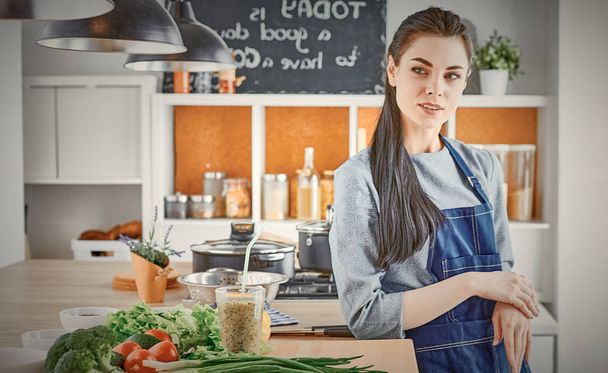 Joyeux jeune femme dans la cuisine avec des légumes frais sur la table
 - Photo, image