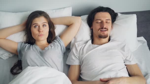 Angry wife covering face with pillow while sleeping husband snoring in bed - Materiał filmowy, wideo