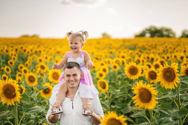 father holding a daughter on his shoulders. Sunflower field. Con - Foto, Bild