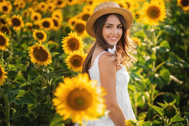Young woman in straw hat at sunflower field. She smiling and her - Photo, Image